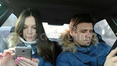 穿着蓝色羽绒服的黑发男人和女人坐在车里看手机里的东西。